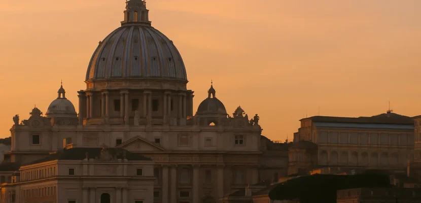 Basílica de São Pedro no Vaticano ao pôr do sol, com céu alaranjado ao fundo.